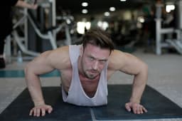 Man performing push-ups on an exercise mat in a busy fitness gym